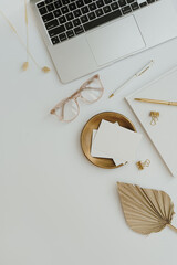 Flatlay of laptop computer, blank paper card sheet, glasses, fan leaf, golden accessories on white background. Top view minimalist aesthetic workspace, business concept. Copy space