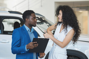 Woman customer enjoys African American salesman offer and presentation of newest car. Black-haired...