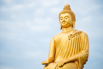 A golden Buddhist deity donation statue against a clear blue sky.