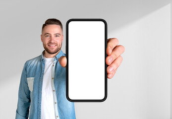 Fototapeta na wymiar Young man showing large phone blank display on light background