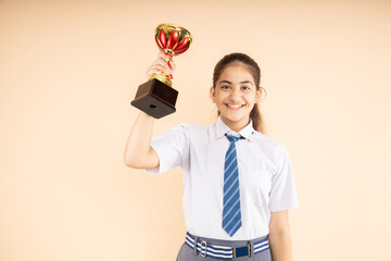 Happy Indian student schoolgirl hold victory trophy in hand isolated on beige background, Studio shot, closeup, Education concept.
