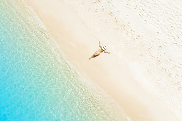 Aerial view with tourist woman sunbathing as laying on the  beach, blue sea water in background...