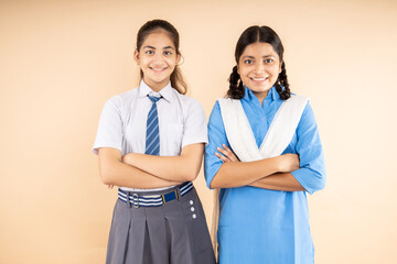 Happy Rural and Modern Indian student schoolgirls wearing school uniform standing together cross arms isolated over beige background, Closeup, Studio shot, Education concept.