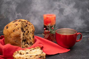 Delicious Panettone with chocolate chips accompanied by a candle and cup of tea on dark background 