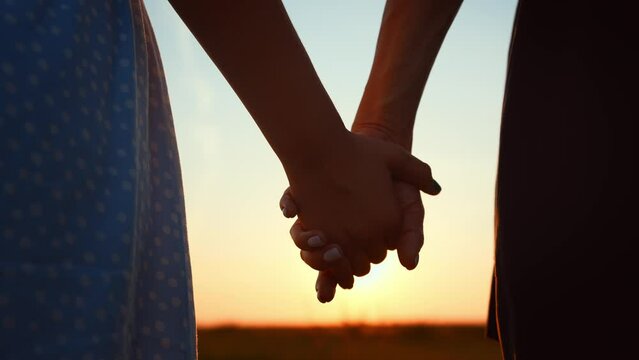 Close-up romantic view of couple holding hands against blurred sky and sunset. Relationships, support and love. Overcoming difficulties. Happy family travel. Date on outdoors nature landscape.