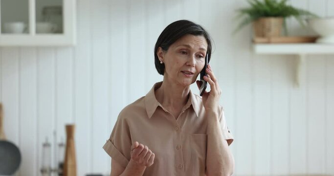 Smiling mature woman blab on phone in kitchen, enjoy pleasant conversation, personal talk using modern smartphone, makes call to online e-services ordering products remotely. Tech, routine, roaming