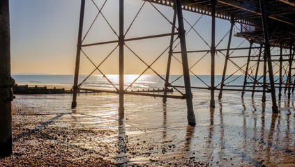 Sunrise viewed from under a pier with reflections on the beach.