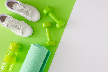 Creative sports concept. Top view photo of dumbbells, exercise mat, white sports shoes and bottle...