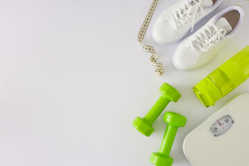 Slimming concept. Flat lay composition of scales green dumbbells sports shoes bottle of water and...