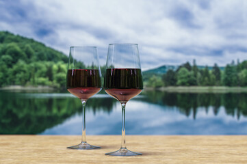 Two glasses of red wine with lake in a forest background.