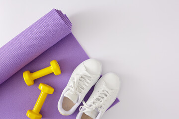 Creative sports concept. Top view photo of yellow dumbbells, violet exercise mat and white sports shoes on white background with copy space. Minimal fitness idea.