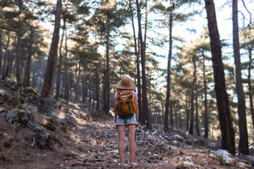 A woman with a backpack and a straw hat on a mountain path