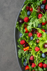 Delicious light salad of arugula and fresh sweet berries, black and red cherries and gooseberries, blueberries and raspberries