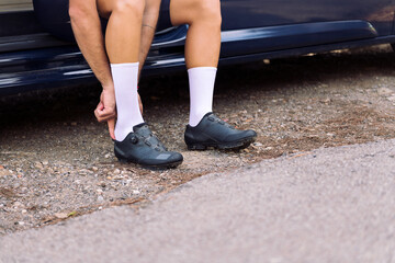 unrecognizable young man putting on cycling shoes sitting on his camper van to go training with his...
