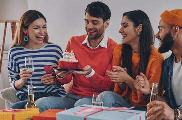 Handsome young man holding birthday cake while celebrating together with friends