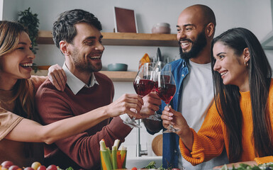 Cheerful young people toasting with wine while having dinner at home together