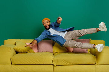 Excited young man using remote control while jumping on the couch against green background