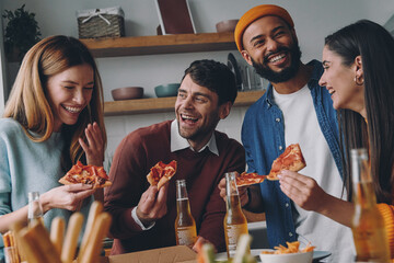 Cheerful young people eating pizza and laughing while enjoying fun time together