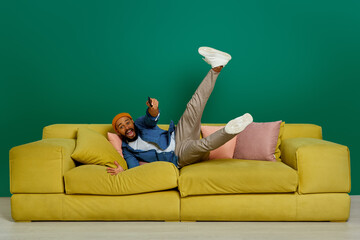 Happy young man using remote control while jumping on the couch against green background