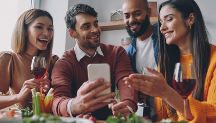 Group of happy young people discussing something while looking at smart phone together