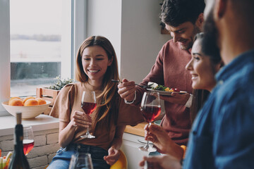 Group of happy young people enjoying food and drinks while having dinner at home together
