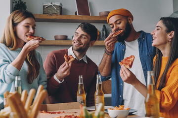 Cheerful young people eating pizza and smiling while enjoying fun time together