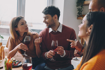 Happy young people drinking wine and talking while enjoying dinner at home together