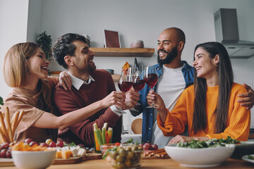 Happy young people toasting with wine while having dinner at home together