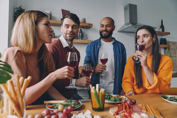 Group of happy young people drinking wine and talking while enjoying dinner at home together