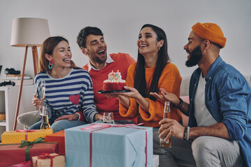 Beautiful young woman holding birthday cake while celebrating together with friends