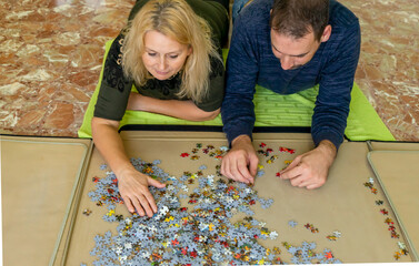Adorable couple doing a puzzle lying on the floor, they enjoy their company while spending some fun time together.