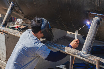 A welder is welding base stand of the old large oil tank to be renovated for a water tank