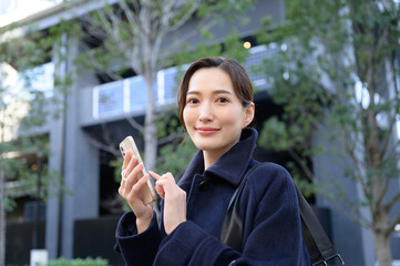 屋外でスーツ姿でスマホをタップする営業のような美しい女性　冬のコート