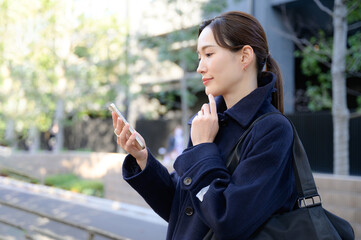 Fototapeta premium 屋外でスーツ姿でスマホをみて場所を探す女性 冬コート