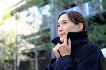 A woman tugging at the collar of her coat because it's winter and she's cold.