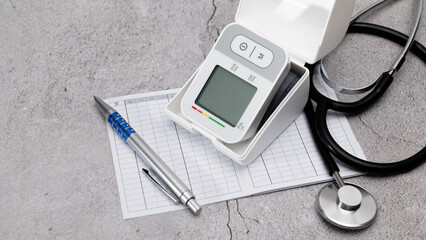 Automatic digital wrist blood pressure monitor; pressure monitoring chart; pen; stethoscope; on gray background