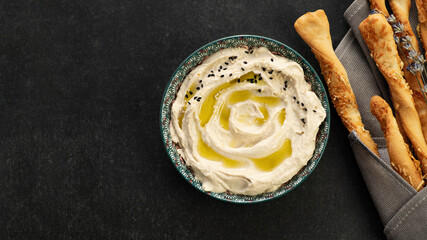 Classic hummus, the finished dish is decorated with sesame seeds and served with grisini bread sticks, top view, banner