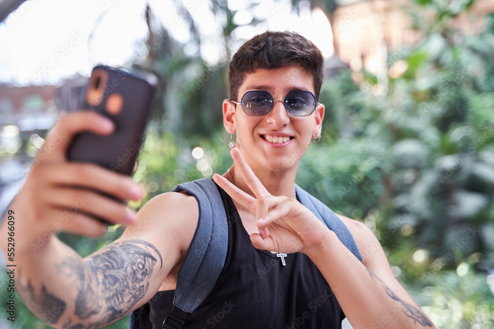 Wall mural portrait of an attractive young tattooed man taking a selfie with his smart phone. man with backpack and sunglasses