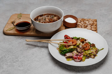 Shrimp udon soup and seafood salad on a gray background. Side view.
