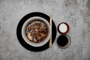 Udon soup with shrimps and a bowl with soy sauce on a gray background. View from above.
