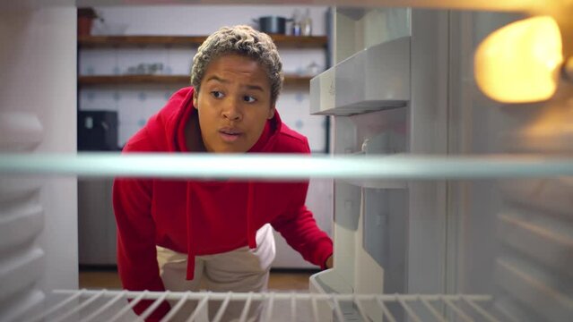 Young African-American woman looks into the empty refrigerator. Realtime