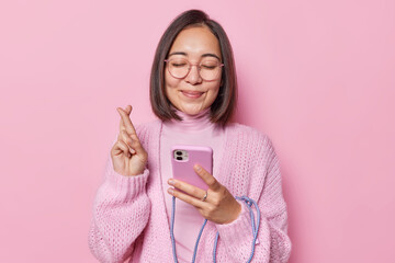 Hopeful Asian woman with dark hair keeps fingers crossed believes in good luck keeps eyes closed...