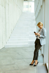 Businesswoman using mobile phone on modern office hallway