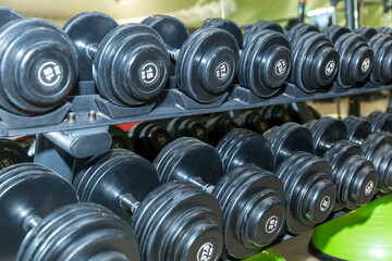 Rows of black dumbbells of different weights in the gym. Sport, activity and health. Close-up.
