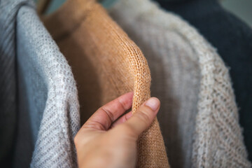 Close-up female hand touching the fabric of a warm sweater, winter clothing quality concept