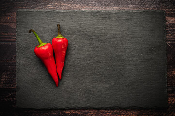 Three hot chili peppers on a slate board on a dark wooden table.
