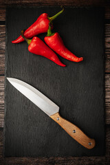 Red hot chili peppers on a slate cutting board on a dark wooden table with a knife. Top down overhead view.