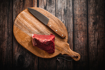 A piece of raw beef on a wooden cutting board with a knife. Wooden table, top down view, flat lay.