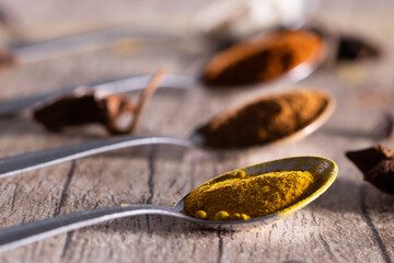 Almonds, cinnamon, paprika and turmeric powder in a spoon on a rustic wooden table.