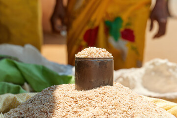 Street market, detail of can in pile of rice in big bag against blurred local woman in background. ...